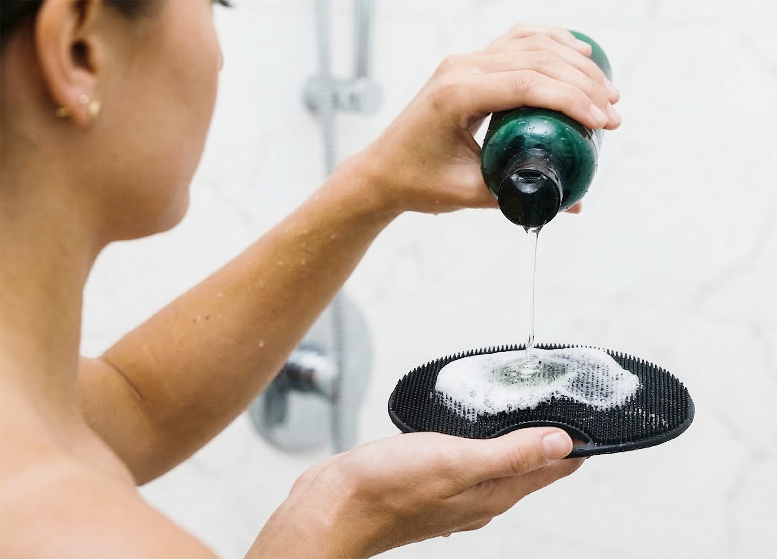 Dispensing body wash onto silicone scrubber with foamy lather in shower.